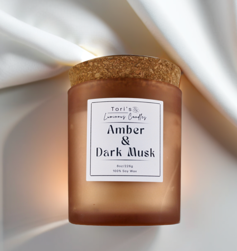 Amber & Dark Musk candle in a frosted amber 8 oz jar and matte cream 12 oz jar, styled on a neutral-toned surface with soft lighting, showcasing the elegant vessels and cozy home décor vibes.