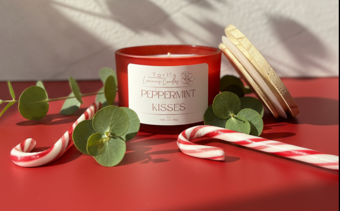Peppermint Kisses candle lit on a clean winter-themed surface, surrounded by red-and-white peppermint candies and soft eucalyptus sprigs. The flame glows brightly, creating a fresh, uplifting holiday feel reminiscent of candy canes and winter air.